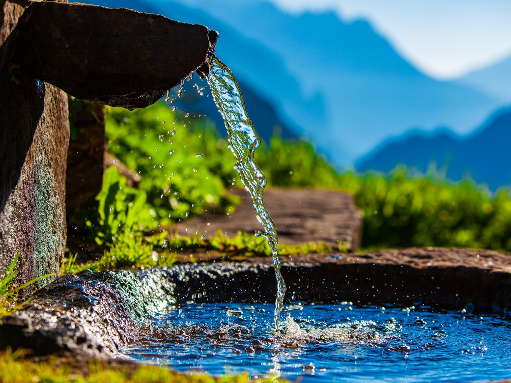 Water pouring from a stone spout into a stone trough, mountains beyond