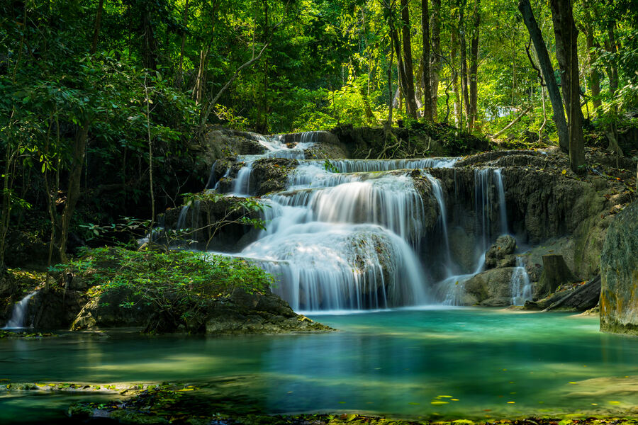 Tiered jungle waterfall cascading over layered mineral rock into a turquoise pool, lush forest above.